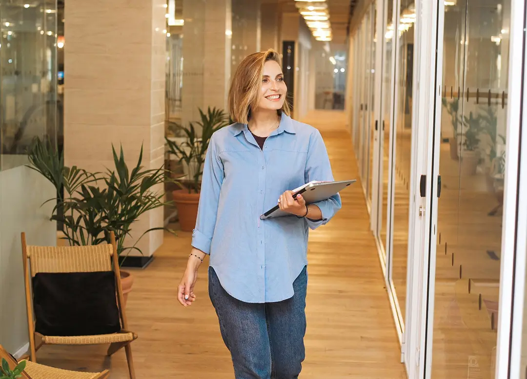 Professional woman walking through a modern office corridor with a tablet